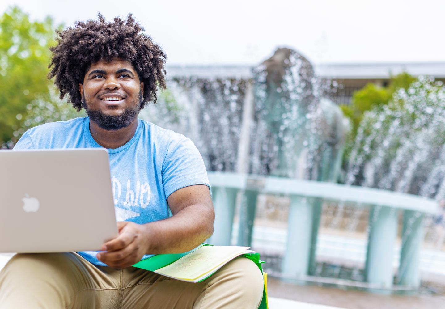 an ODU student is sitting in front of the lion fountain with a laptop