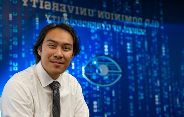 A student sits in front of the "School of Cybersecurity" sign at Old Dominion University.